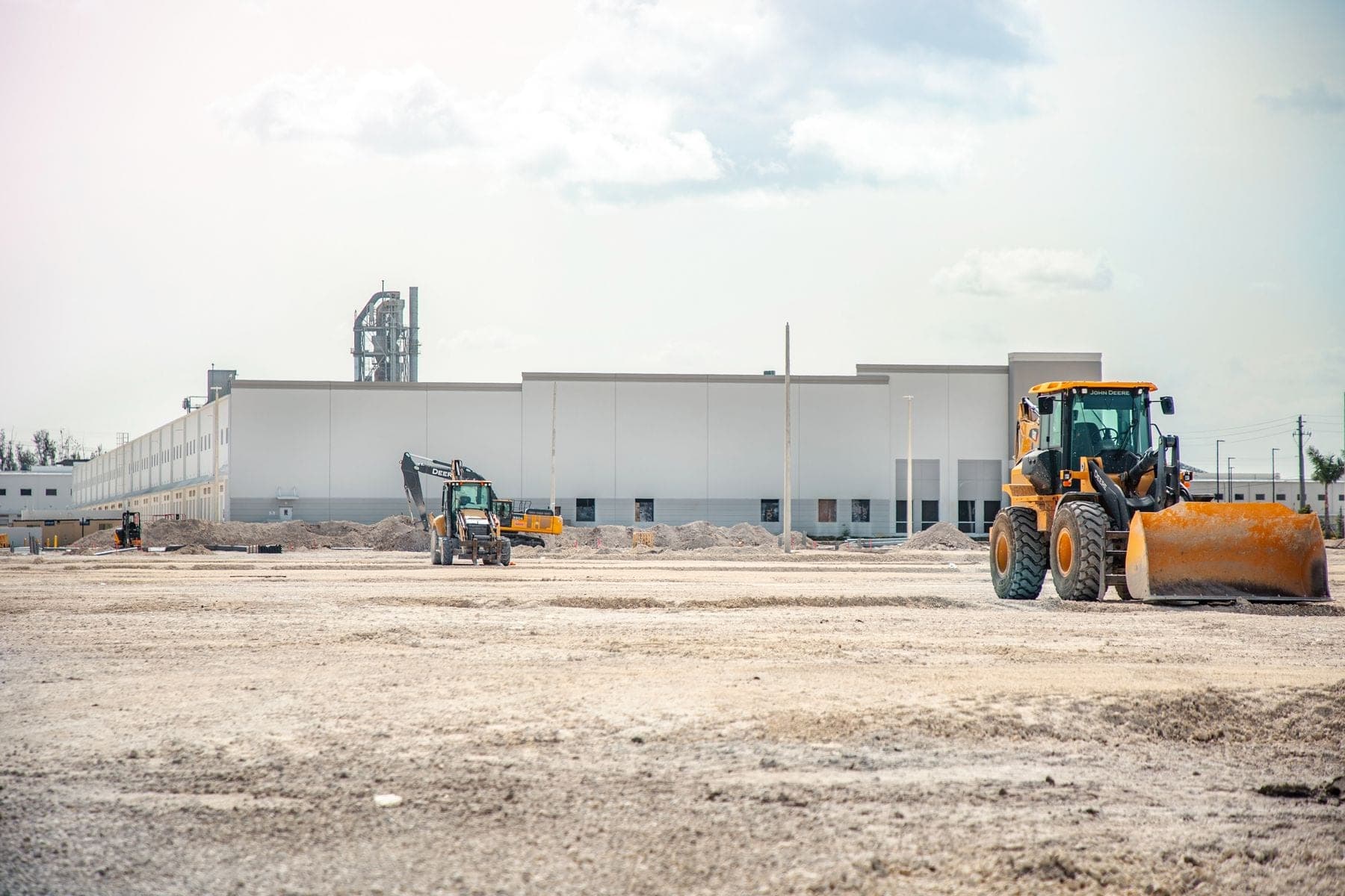 Earthmoving equipment outside an industrial facility under construction.